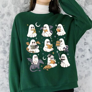 May include: Dark green sweatshirt with a repeating pattern of cartoon ghosts reading books, with bats, dragons, and moons. The ghosts are white with black eyes and are holding books of various colours. The design is repeated across the front of the sweatshirt.