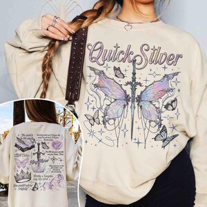 Peut inclure: Un sweat-shirt cr&egrave;me avec un motif de papillon avec une &eacute;p&eacute;e qui le traverse. Le texte "Quick Silver" est imprim&eacute; au-dessus du papillon. Le sweat-shirt a une coupe ample et un col rond.
