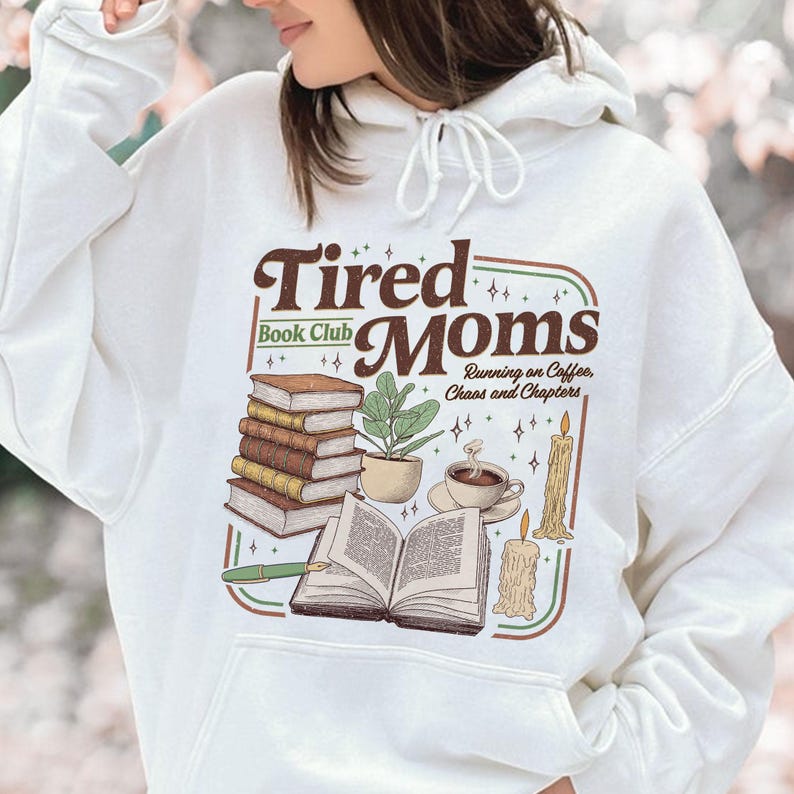 Puede incluir: Sudadera con capucha blanca con un gr&aacute;fico marr&oacute;n y verde que dice "Tired Moms Book Club". El dise&ntilde;o incluye ilustraciones de libros, una planta, caf&eacute; y una vela. Tambi&eacute;n incluye el texto "Running on Coffee, Chaos and Chapters".