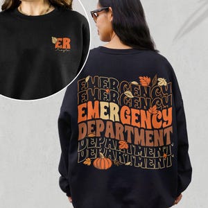 May include: Black sweatshirt with a graphic print of the words "Emergency Department" in a retro style with fall leaves and a pumpkin. The text is repeated multiple times in different sizes and colors.