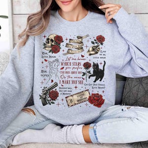 May include: Gray sweatshirt with a graphic print of red roses, a skull, a black cat, and text that reads "Let me know which stars you prefer the ones above you or the ones I make you see".