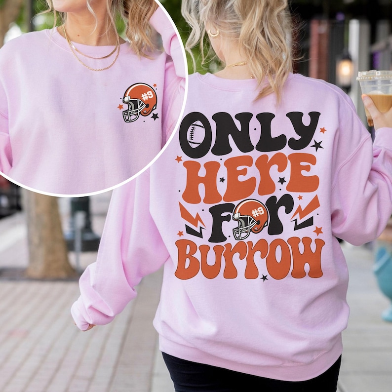 以下が含まれることがあります： オレンジと黒の「ONLY HERE FOR BURROW」の文字とフットボールヘルメットのグラフィックがプリントされたピンクのトレーナー。トレーナーの背面には、フットボールヘルメットのグラフィックと番号9がプリントされています。