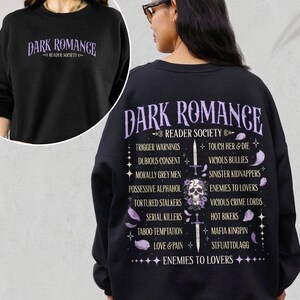 May include: Black sweatshirt with the text "DARK ROMANCE READER SOCIETY" in purple. The back features a skull with a sword and a list of dark romance tropes in purple, including "Enemies to Lovers" and "Trigger Warnings".