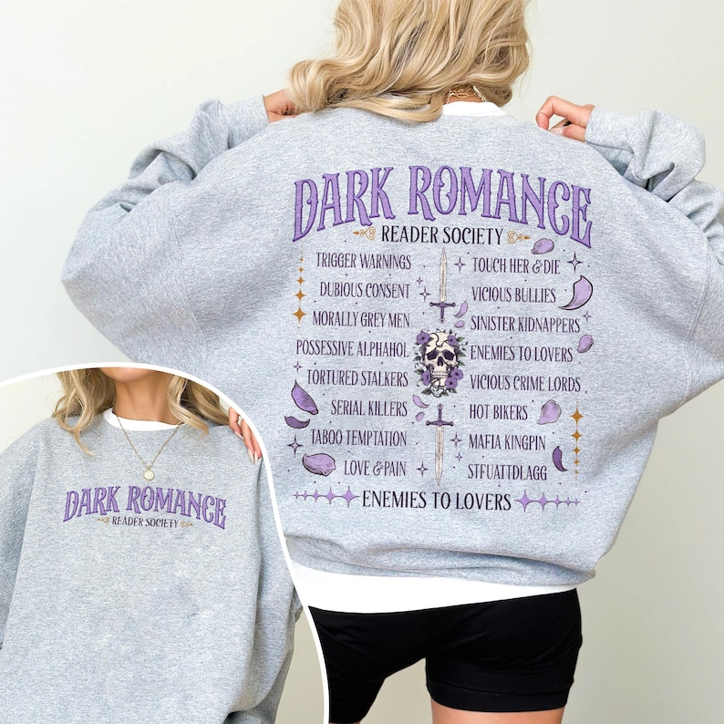 May include: A light gray sweatshirt with the text "DARK ROMANCE READER SOCIETY" in purple. The back of the sweatshirt features a list of dark romance tropes and a skull graphic. The sweatshirt is made of a soft material.