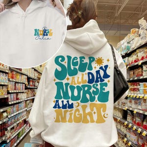 May include: White hoodie with a blue and yellow graphic that says "Sleep All Day Nurse All Night". The hoodie also has a smaller graphic that says "Nurse Julia".