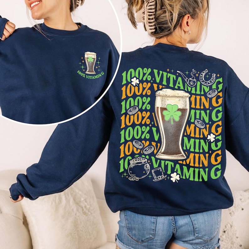 Puede incluir: Sudadera azul marino con un dise&ntilde;o de vaso de cerveza y el texto "100% Vitamin G" en la parte delantera. La parte trasera presenta un dise&ntilde;o m&aacute;s grande con un vaso de cerveza, tr&eacute;bol y texto en verde y naranja.