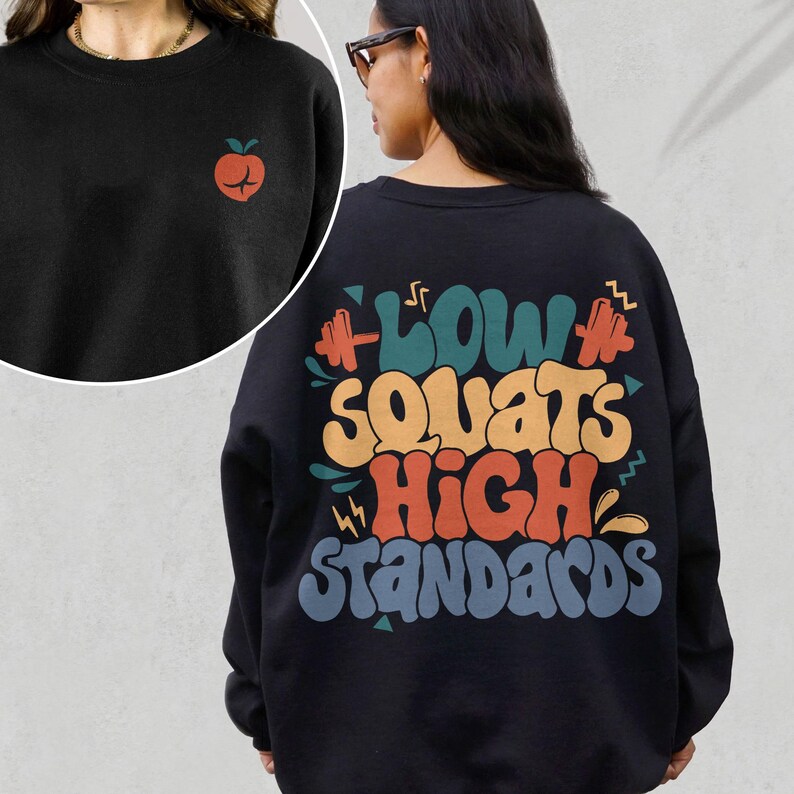 May include: Black sweatshirt with a retro-style graphic on the back that says "Low Squats High Standards" with a dumbbell icon on either side of the text. The graphic is in shades of orange, yellow, blue, and green.