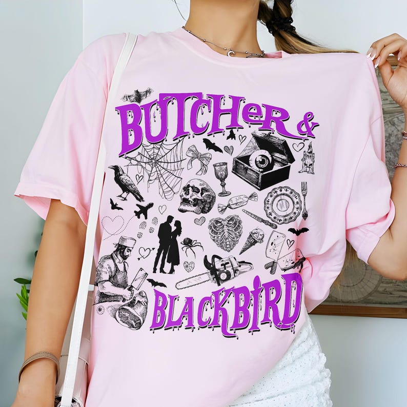 May include: A light pink t-shirt with the words "BUTCHER & BLACKBIRD" in purple, along with various black and white illustrations. The illustrations include bats, a spiderweb, a skull, and a chainsaw.