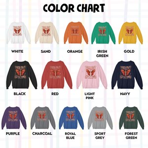 May include: Color chart showing 12 different colors of a sweatshirt with a graphic print of a winged sword and the text "VIOLENT LITTLE THINGS". The colors are white, sand, orange, Irish green, gold, black, red, light pink, navy, purple, charcoal, royal blue, sport grey, and forest green.