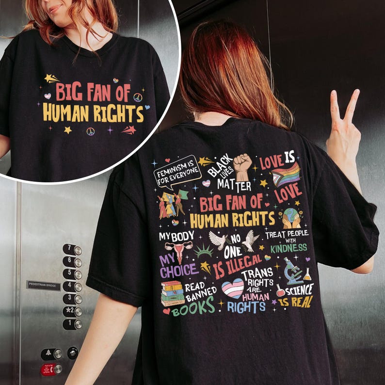 May include: A black t-shirt featuring a graphic print on the back with various colorful illustrations and text including "Big Fan of Human Rights," "Feminism is for Everyone," "Black Lives Matter," "My Body My Choice," and "Trans Rights are Human Rights."