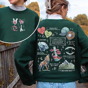 K&ouml;nnte beinhalten: Gr&uuml;ner Sweatshirt mit einem grafischen Druck aus verschiedenen Bildern und Text. Der Text enth&auml;lt Zitate aus dem Buch "Twilight" von Stephenie Meyer. Die Bilder beinhalten einen Diamanten, einen Wolf, ein Schachbrett, ein Herz, eine Baseballkappe, einen Baseballhandschuh und eine Bergkette.