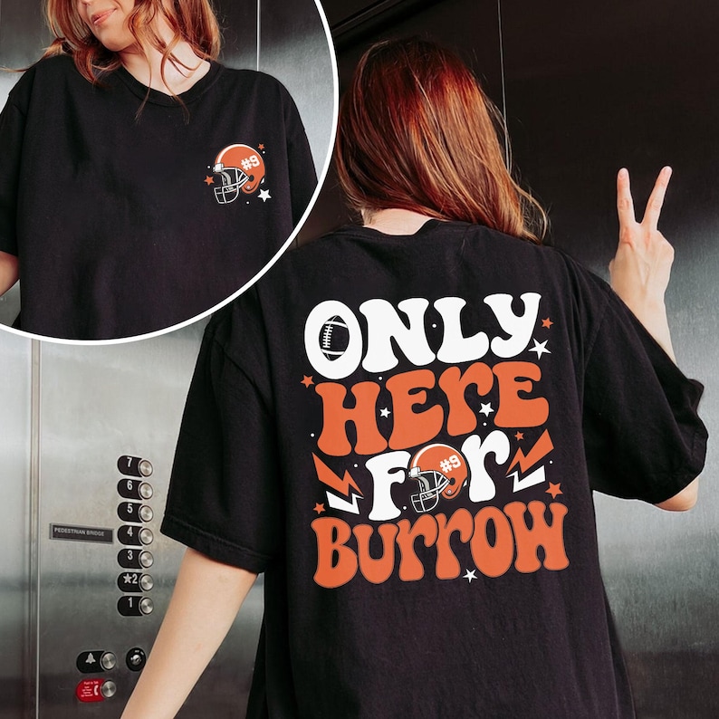 以下が含まれることがあります： 前面にフットボールのヘルメットのグラフィック、背面に「ONLY HERE FOR BURROW」の文字が入った黒いTシャツ。文字はレトロなフォントで、オレンジと白の色を使用しています。