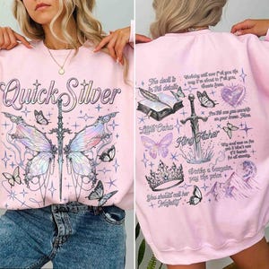 Peut inclure: Sweat-shirt rose avec un imprim&eacute; graphique d'un papillon, d'une &eacute;p&eacute;e et d'une couronne. Le texte "Quick Silver" est imprim&eacute; sur le devant du sweat-shirt. Le texte "King Fisher" est imprim&eacute; sur le dos du sweat-shirt.