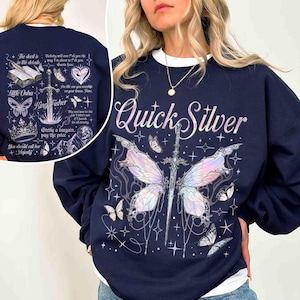Peut inclure: Un sweat-shirt bleu marine avec un imprim&eacute; graphique d'un papillon aux ailes iris&eacute;es et d'une &eacute;p&eacute;e. Le texte "Quick Silver" est imprim&eacute; dans une police de caract&egrave;res stylis&eacute;e au-dessus du papillon.