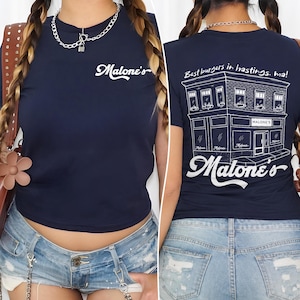 May include: Navy blue t-shirt with the text "Malone's" in white script on the front. The back of the shirt features a detailed white illustration of a restaurant with the text "Best burgers in hastings, ma!" and "Malone's".