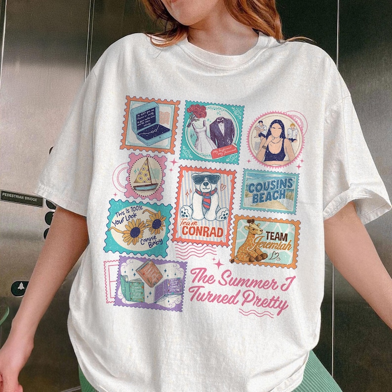 May include: White t-shirt featuring colorful postage stamp designs. Stamps include a laptop, wedding attire, a woman, a pizza, a bear, sunflowers, a giraffe, and books. Text on the shirt reads "The Summer I Turned Pretty", "Team Conrad", and "Cousins Beach".