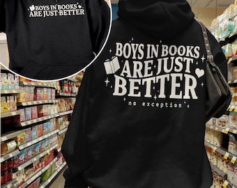May include: Black hoodie with the text "BOYS IN BOOKS ARE JUST BETTER" in white. The hoodie has a front pocket and a hood. The text is accompanied by a book and heart graphic. The phrase "no exception" is also printed on the back.