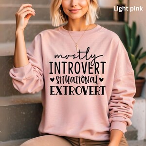 Può includere: Felpa rosa chiaro con la scritta nera "mostly INTROVERT situational EXTROVERT". La felpa è di colore rosa chiaro tinta unita e ha un girocollo. Il testo è centrato sul davanti.