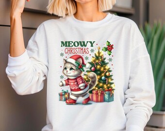 Peut inclure: Sweat-shirt blanc avec un motif festif "Meowy Christmas". Le motif représente un chat de dessin animé portant un bonnet et un pull de Père Noël, marchant près d'un sapin de Noël décoré et de cadeaux emballés. Le mot "WHITE" est imprimé en haut à droite.