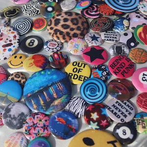 May include: A collection of colorful pinback buttons with various designs. Some buttons feature text like "Out of Order" and "Being Kind is Punk." Other designs include a smiley face, a leopard print, and a black star.