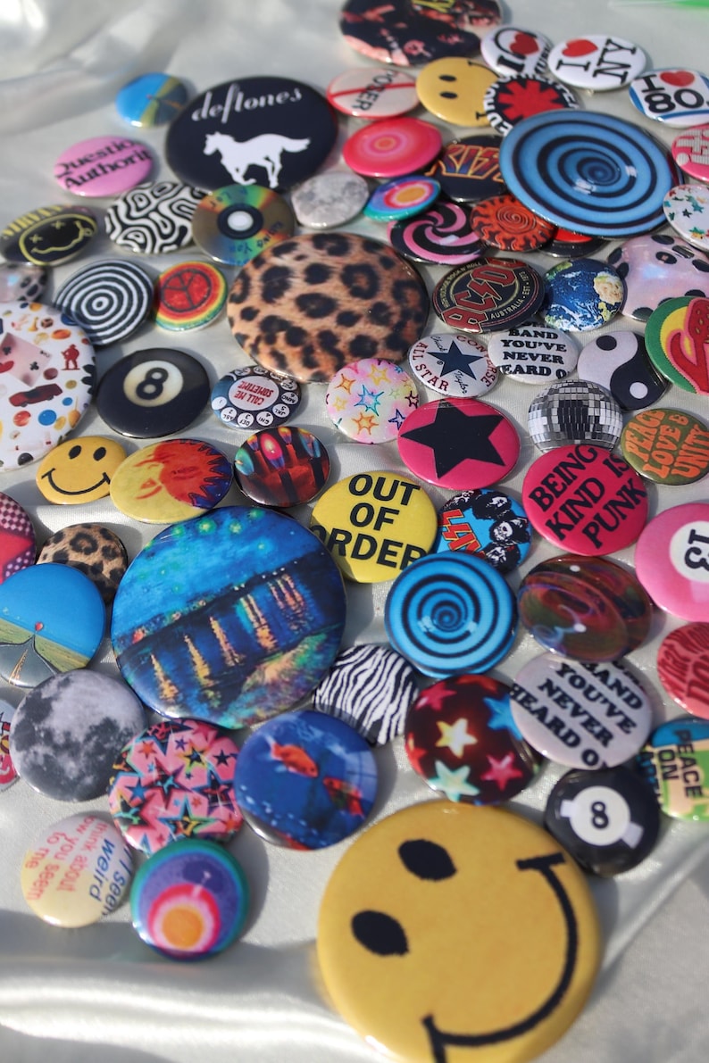 May include: A collection of colorful pinback buttons with various designs. Some buttons feature text like "Out of Order" and "Being Kind is Punk." Other designs include a smiley face, a leopard print, and a black star.