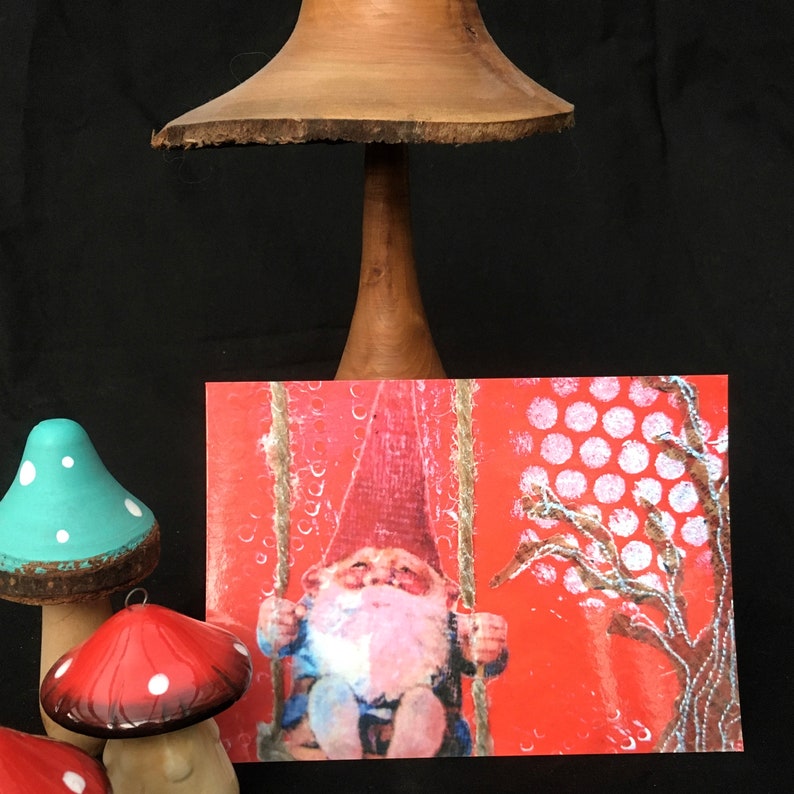 Puede incluir: Una tarjeta roja con un patr&oacute;n de lunares blancos y un &aacute;rbol blanco con un gnomo en un columpio. El gnomo lleva un gorro rojo y tiene una barba blanca. La tarjeta tiene el texto "The Gnome on the Swing".