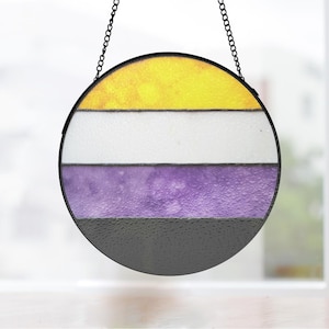 Puede incluir: Una ventana redonda de vitrales colgando de una cadena negra. La ventana está dividida en cuatro bandas horizontales de amarillo, blanco, morado y negro.