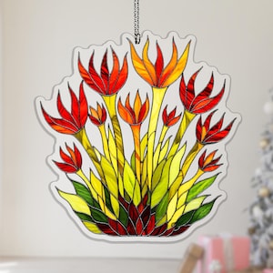 May include: A stained glass ornament featuring a bouquet of stylized flowers. The flowers have red and orange petals, yellow stems, and green leaves. The ornament is hanging from a chain.