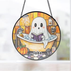 Op de afbeelding: Ronde Halloween-decoratie met een cartoongeest in een badkuip die een boek leest. De scène bevat bubbels, een pompoen en een schedel. De naam "John" staat onderaan de afbeelding.