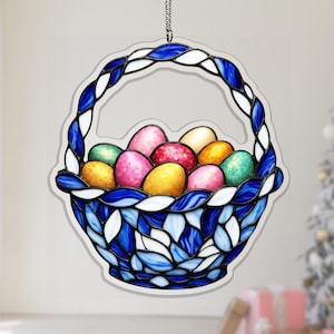 Könnte beinhalten: Ein Buntglas-Osterkorb gefüllt mit bunten Eiern. Der Korb ist blau und weiß mit einem geflochtenen Griff. Die Eier sind in verschiedenen Farben, darunter rosa, gelb, grün und rot. Der Korb hängt an einer silbernen Kette.