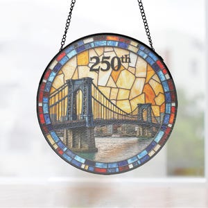 Pode incluir: Janela redonda de vitral com uma cena de ponte com o texto "250th". A janela tem uma borda de mosaico de azulejos azuis, vermelhos e brancos. A ponte é detalhada com uma paisagem urbana ao fundo, suspensa por uma corrente preta.