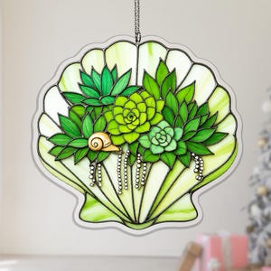 May include: Stained glass seashell with a cluster of green succulents and a small snail. The shell is a light green with darker green accents. The succulents are various shades of green. Decorative hanging art.