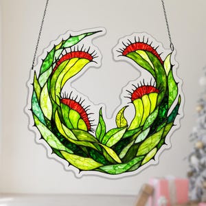 Puede incluir: Un diseño de vidriera de una Venus atrapamoscas, con hojas verdes vibrantes, acentos amarillos y trampas rojas. La obra de arte está suspendida por una cadena, mostrando un tema botánico único. El diseño es circular.