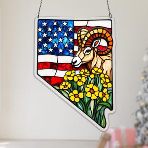 May include: Stained glass art piece in the shape of Nevada, featuring the American flag, a ram, and yellow flowers. The artwork is suspended by a chain.