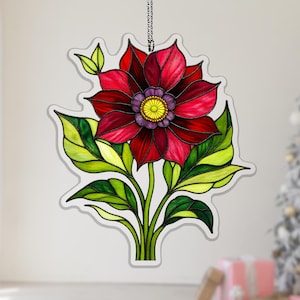 May include: A stained glass flower decoration featuring a large red flower with a yellow and purple center, green leaves, and a white outline. The flower is suspended by a silver chain, suitable for hanging.