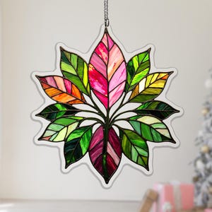May include: A stained glass leaf decoration with a starburst shape. The leaves are a mix of green, pink, orange, and yellow. The piece is hanging from a chain. The background is a soft white.