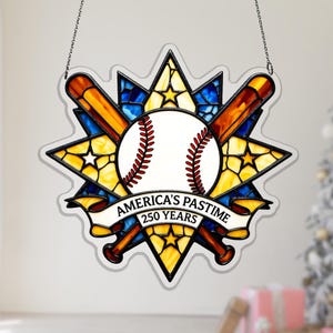 Può includere: Decorazione a tema baseball in vetro colorato con una palla bianca, cuciture rosse e due mazze incrociate. Il design include uno striscione con la scritta "AMERICA'S PASTIME 250 YEARS" ed è circondato da un motivo a stella in vetro giallo, blu e trasparente.