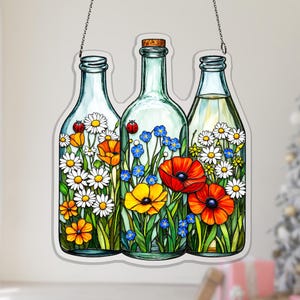 May include: A decorative glass panel featuring three bottle-shaped designs filled with colorful flowers. The bottles are filled with daisies, poppies, and other wildflowers, with a ladybug on two of the bottles. The panel hangs from a chain.