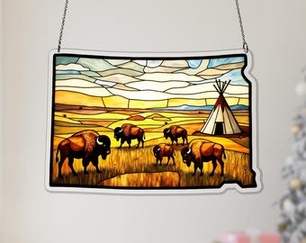 May include: A stained glass panel depicting a prairie scene with bison and a teepee. The artwork is in the shape of a state, with a white border and a chain for hanging. The colors include shades of brown, yellow, and blue.