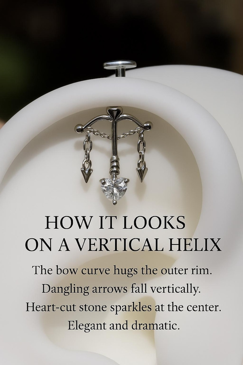 Puede incluir: Un pendiente vertical de h&eacute;lice plateado con un dise&ntilde;o de arco, flechas colgantes y una piedra en forma de coraz&oacute;n. El texto dice: "HOW IT LOOKS ON A VERTICAL HELIX". La curva del arco abraza el borde exterior. Las flechas colgantes caen verticalmente. La piedra en forma de coraz&oacute;n brilla en el centro. Elegante y dram&aacute;tico.