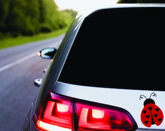 May include: A white car with a red ladybug sticker on the back window. The ladybug has black spots and a black outline.
