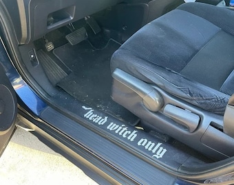 May include: A close-up of a car's interior door sill with a black and white graphic that reads "Head Witch Only".