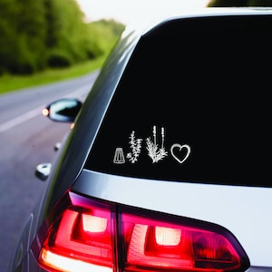 Könnte beinhalten: Ein weißes Auto mit einer schwarzen Heckscheibe. Die Heckscheibe hat einen weißen Aufkleber mit einem Salzstreuer, drei Kräuterzweigen und einem Herzen.