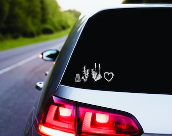 May include: A white car with a black rear window. The rear window has a white decal with a salt shaker, three sprigs of herbs, and a heart.