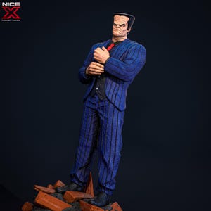 May include: A blue and black striped suit with a red tie. The suit is worn by a figure with a flat top haircut and a serious expression. The figure is standing on a pile of broken bricks.