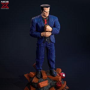 May include: A blue and black pinstripe suit figure with a bald head and a red tie. The figure is standing on a pile of broken bricks with a red and black spider figure in the background.
