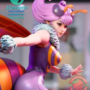 May include: A purple and yellow bee-themed figurine with a fluffy white collar and antennae. The figurine has a large, round head with a pink wig and a friendly expression. The figurine is wearing a purple and yellow jumpsuit with a bee pattern. The figurine is standing on a white surface. The text "Lychee Slicer Ambassador" is visible on the figurine's leg.