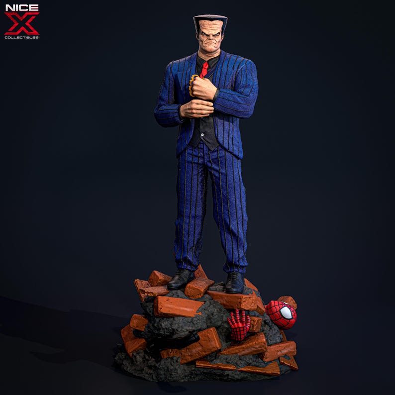 May include: A blue and black pinstripe suit figurine standing on a pile of broken bricks. The figurine has a bald head and a serious expression. A red spider-man figure is lying on the bricks.