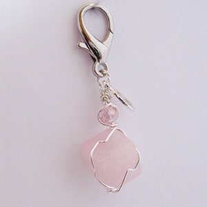 May include: A rose quartz charm with a silver-colored lobster clasp. The charm features a raw, light pink rose quartz stone encased in a silver wire frame, with a small pink bead and a decorative silver leaf charm.