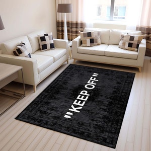 Puede incluir: Alfombra de área negra y blanca con el texto "KEEP OFF" en letras blancas sobre fondo negro. La alfombra tiene un aspecto desgastado y vintage.